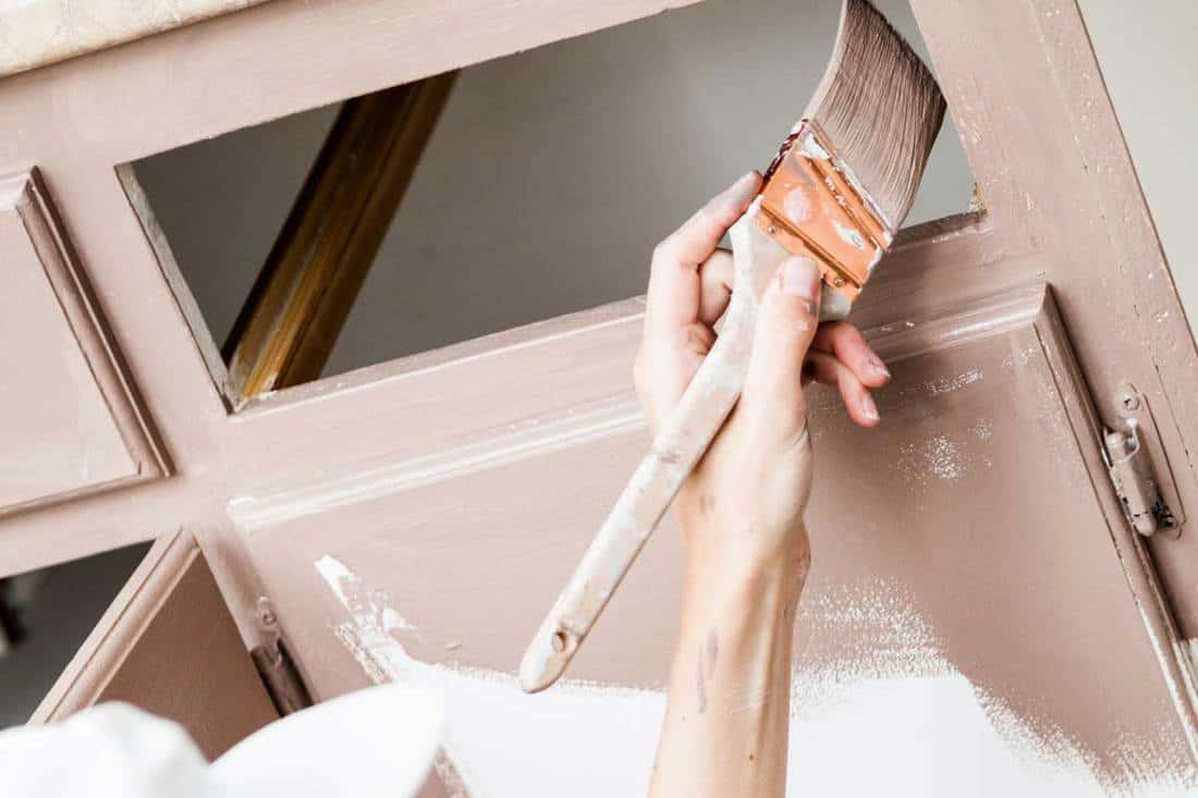 Close up of woman painting cabinets, How Many Coats Of Primer And Paint For Bathroom Cabinets?