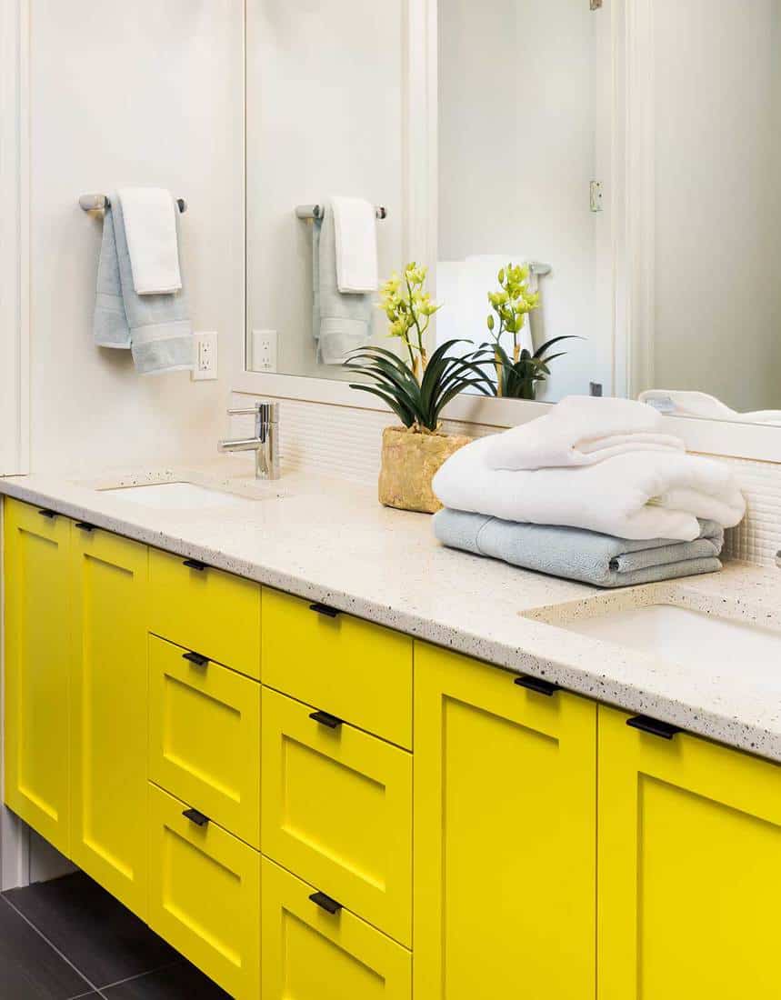 Detail close up of sink, faucet, countertop, yellow cabinets and mirror