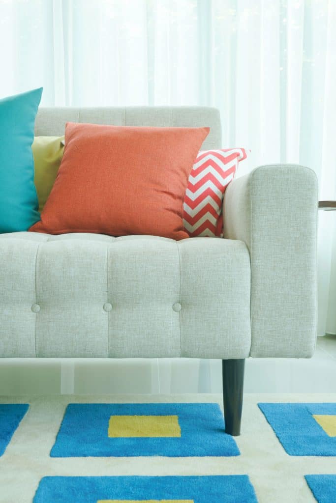 Different colored throw pillows on a sectional with small blue rugs underneath