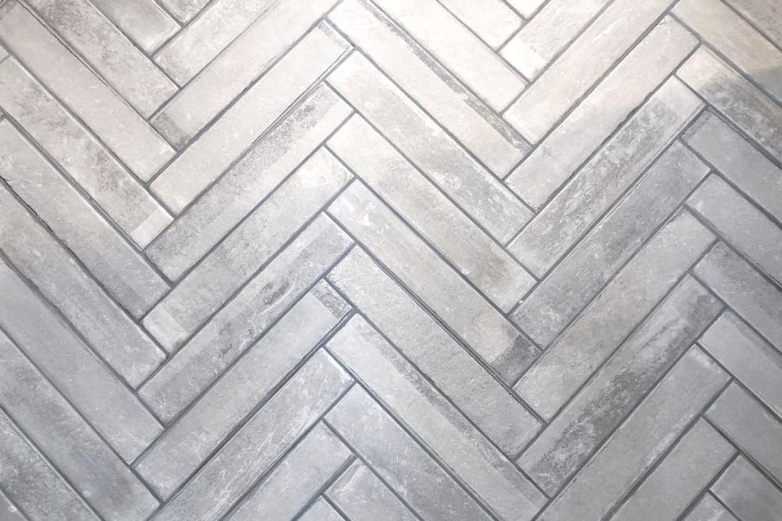 Gray bathroom tiles placed in a zigzag pattern, Is Bathroom Grout Waterproof Or Porous? [And Should You Seal It?]