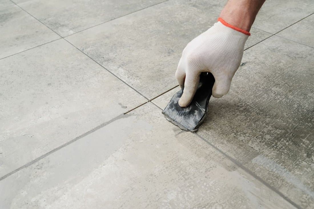 Grouting ceramic tiles. Tilers filling the space between tiles using a rubber trowel.