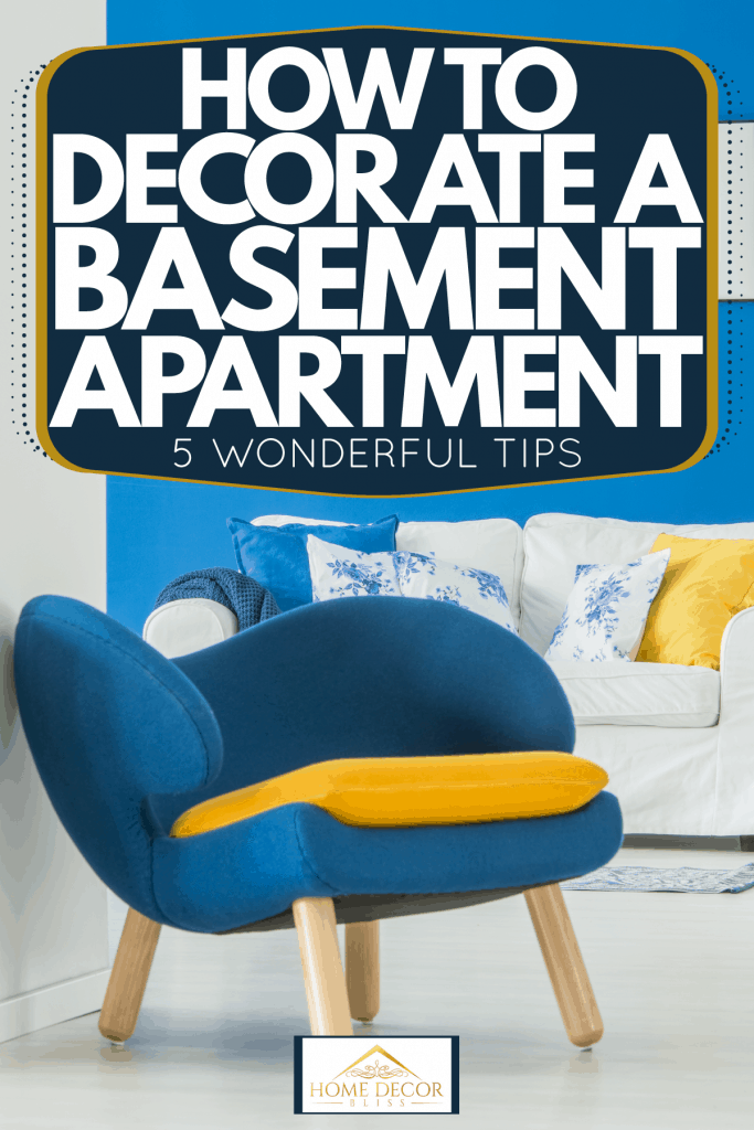 A lively and beautiful white living room with a blue accent wall, white loveseat sofa, and a small blue accent chair, How To Decorate A Basement Apartment [5 Wonderful Tips]