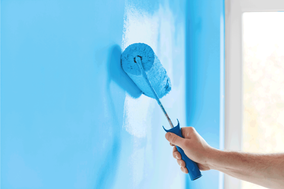 Male hand painting wall with paint roller. Painting apartment, renovating with blue color paint