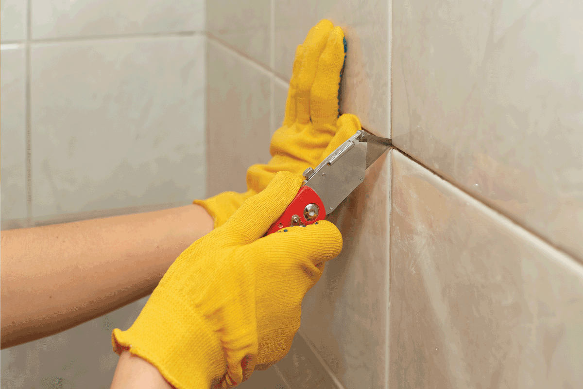 Male hands with knife removing the old grout. Replacing old grout between tiles. How To Remove Grout From Bathroom Tiles In 5 Easy Steps