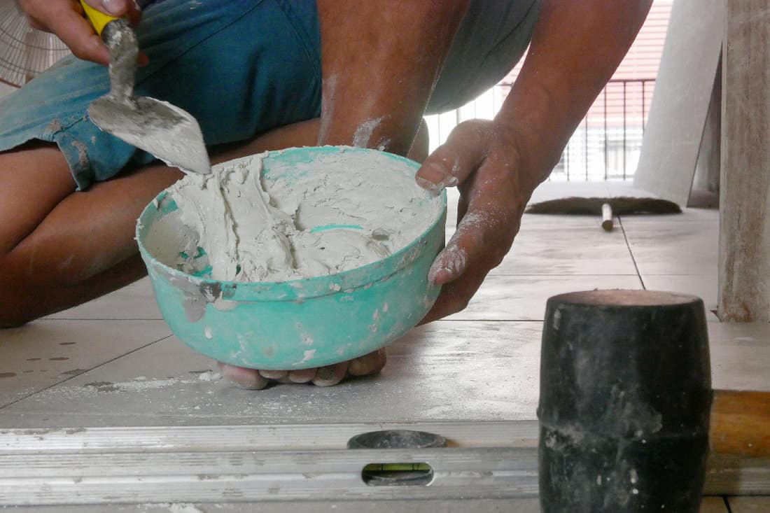 Mixed tile grout in a plastic bowl in a construction worker's hands ready to be used for grouting ceramic tile floor