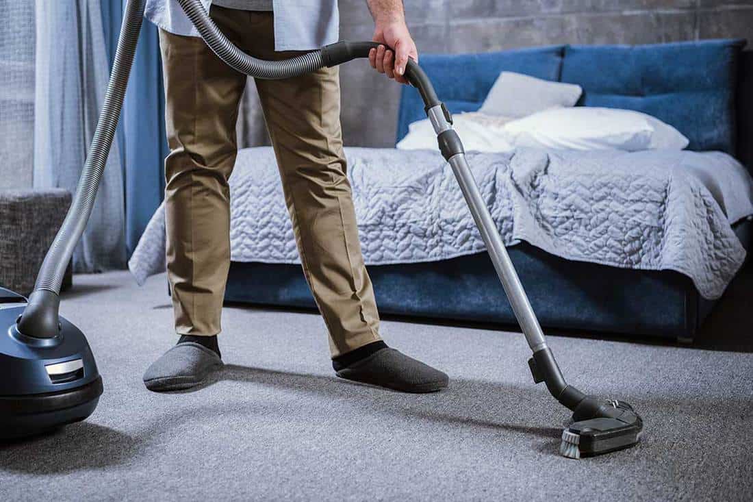 Partial view of man with vacuum cleaner cleaning carpet in bedroom, How Often Should You Clean Your Bedroom?