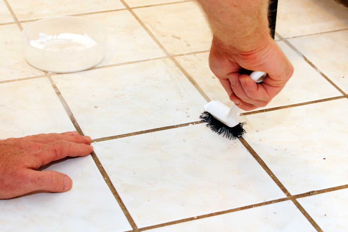 Person cleaning grout with brush, How To Clean Black Grout In A Bathroom