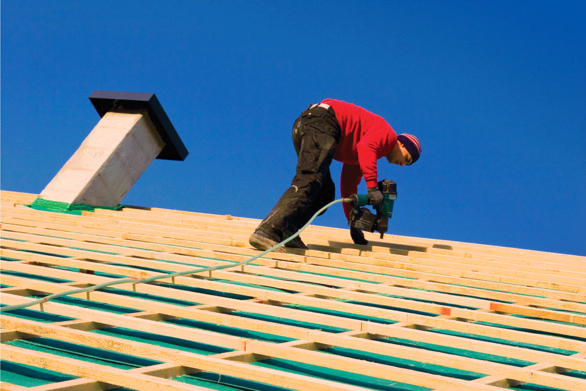 Tilt view of a carpenter on a roof, against blue sky, carpenter building a tile batten construction for roof tiles, using a pneumatic nail gun. 5 Of The Best Nail Guns For Wood Framing