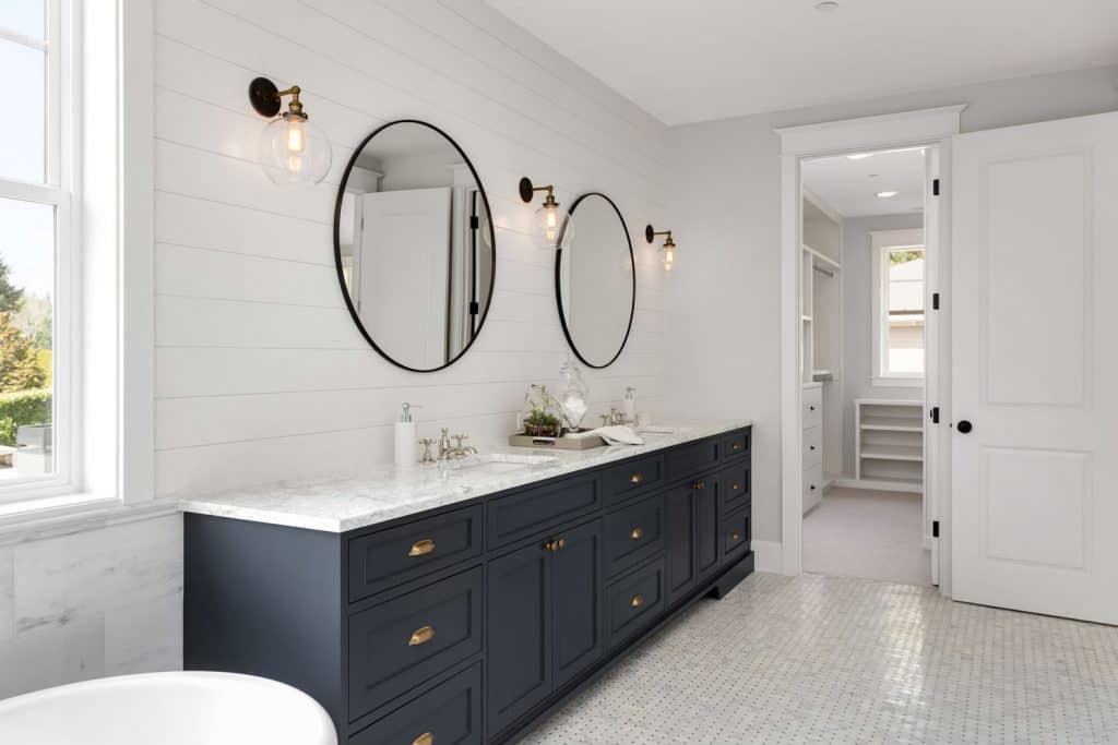 Ultra modern bathroom painted in white tiles, round mirrors, white gray cabinetry in the vanity section, and small lamps on the walls