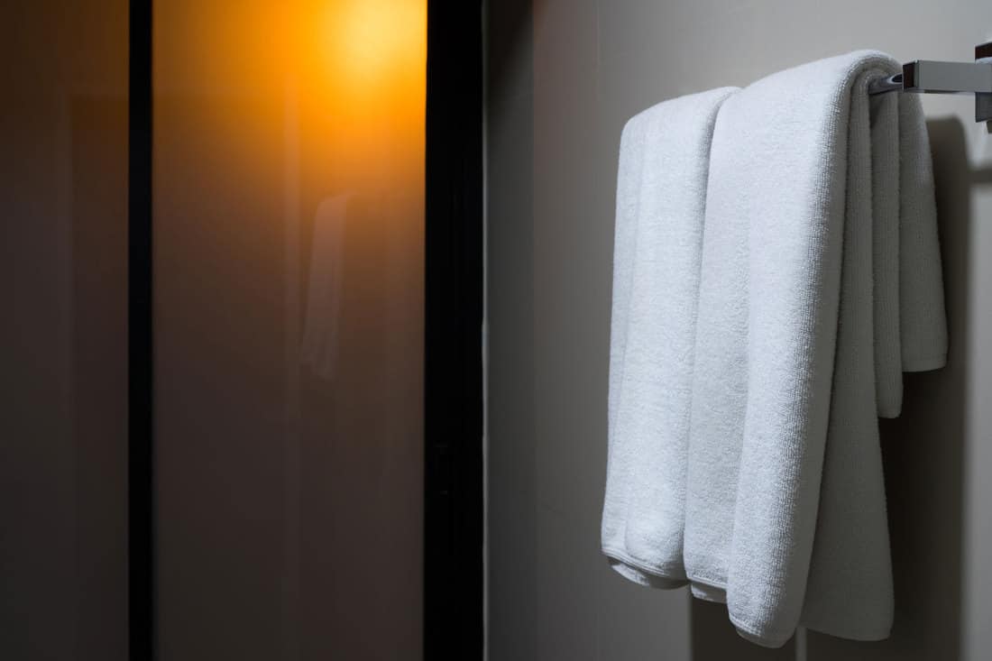White towels hanged on a towel hanger inside an unlit bathroom, Where To Hang Wet Towels After Showering