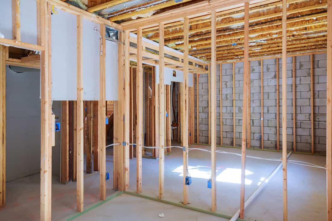 Wooden framing of a basement with visible wiring and unfinished plastered cement, What Wood To Use For Framing A Basement?