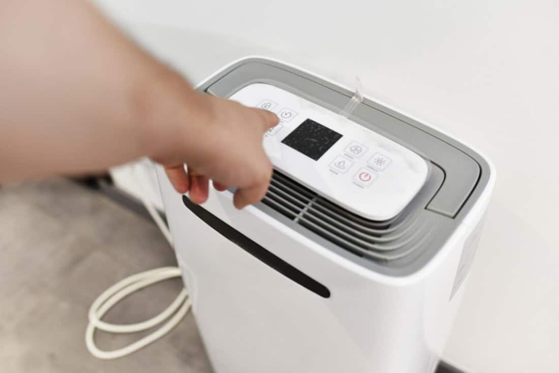 man's hand turning on a dehumidifier in the entrance of a house or office. To prevent joint pain.