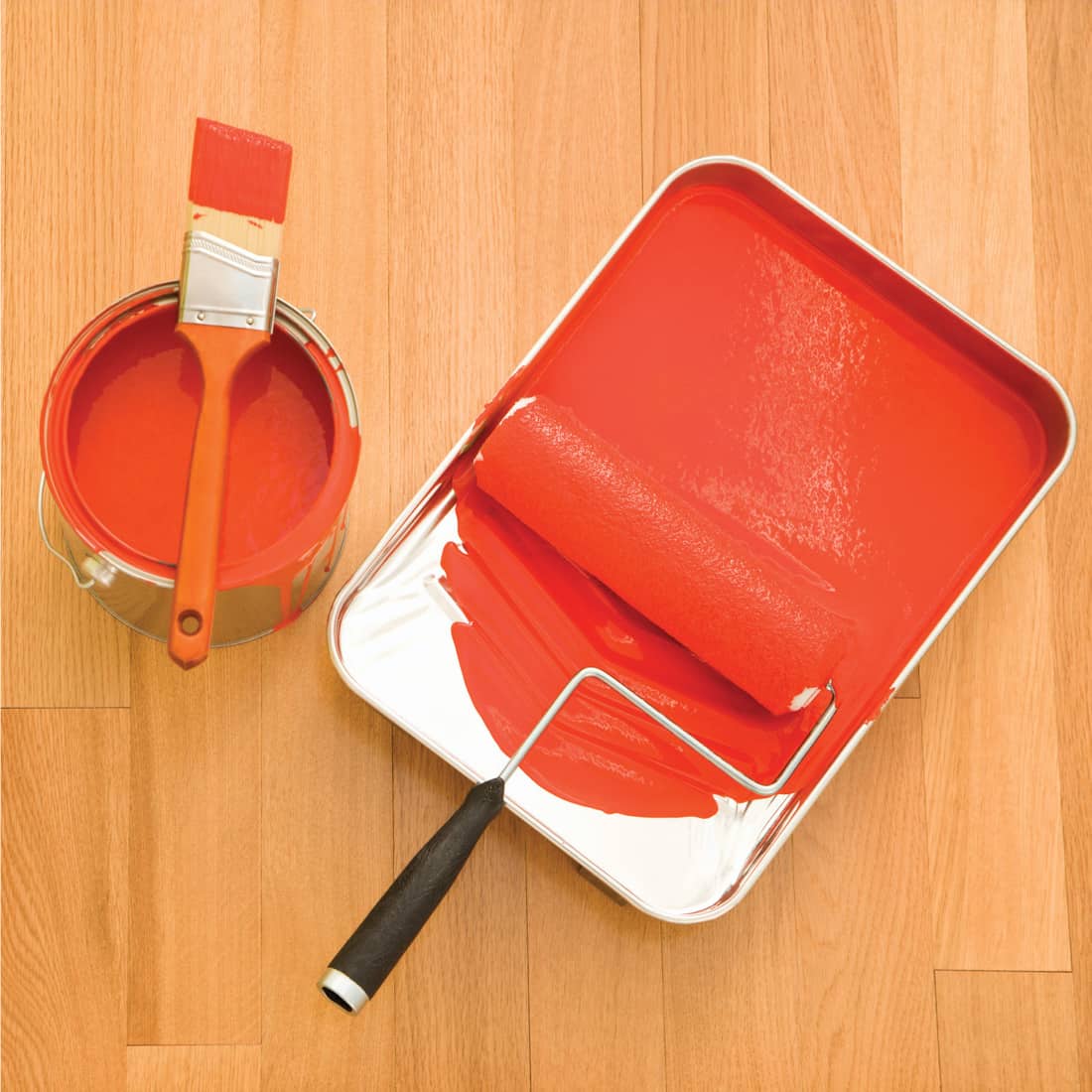 orange paint on paint can and tray with paintbrush and roller