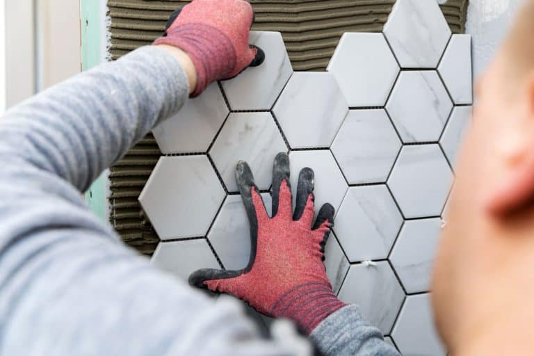 tiling - man laying marble texture hexagon tiles on the wall, Can You Tile Without Grout? [And Here's How]