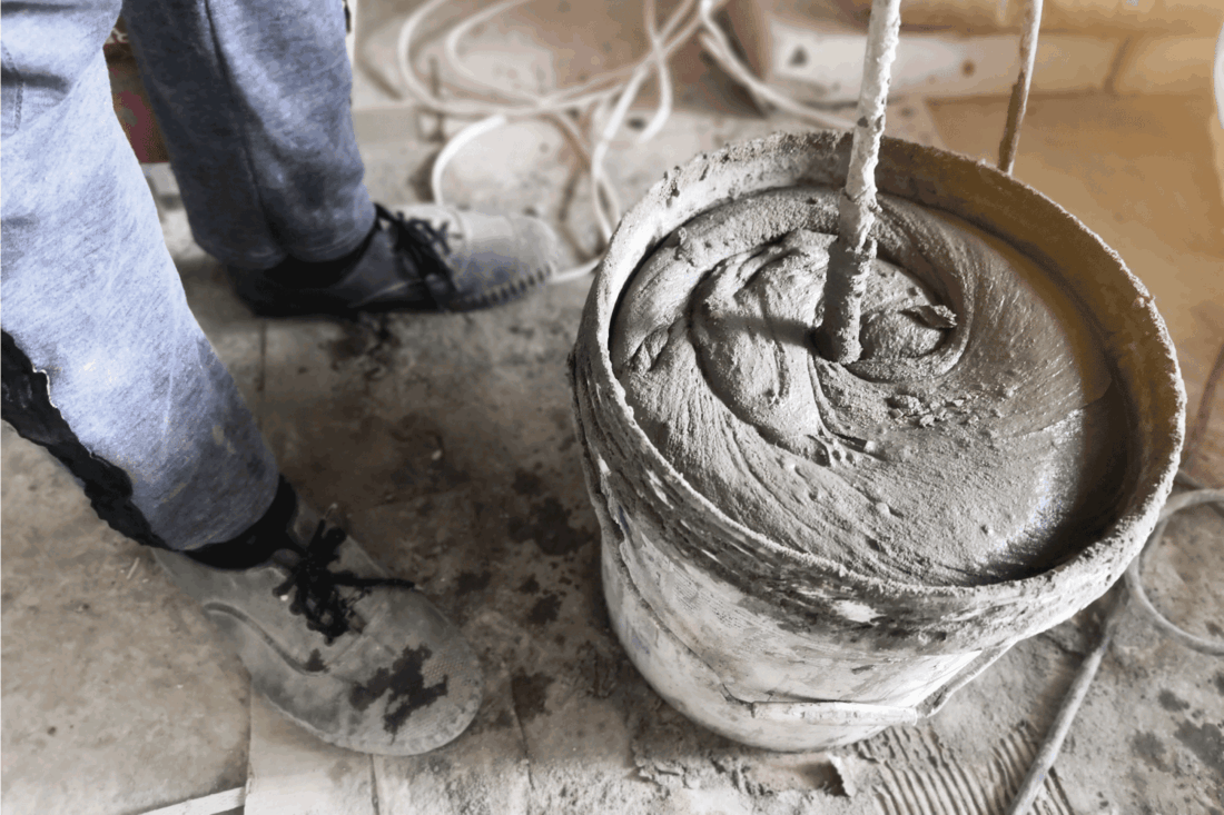 worker hands are mixing concrete in a bucket at a construction site. Mixing cement or mortar with Electric drill.