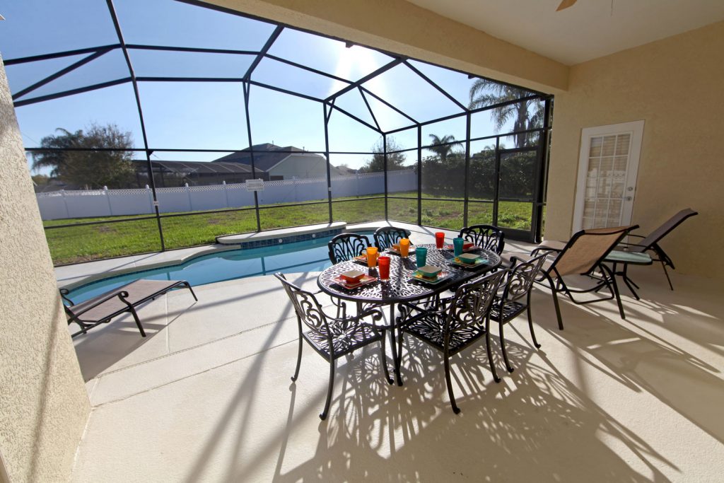 A huge stucco walled lanai with metal dining chairs and a small pool near the window