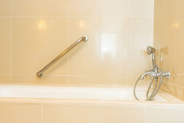 A light yellow tiled shower area with a handle bar and stainless steel fixtures, How High Should Grab Bars Be Installed In A Shower?