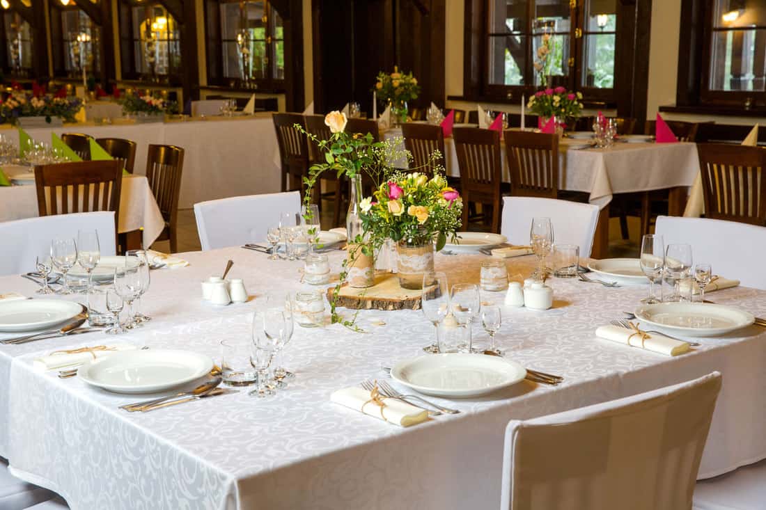 A luxurious restaurant incorporated with white clothing and wooden chairs, How To Choose A Tablecloth Color - Questions To Ask Yourself