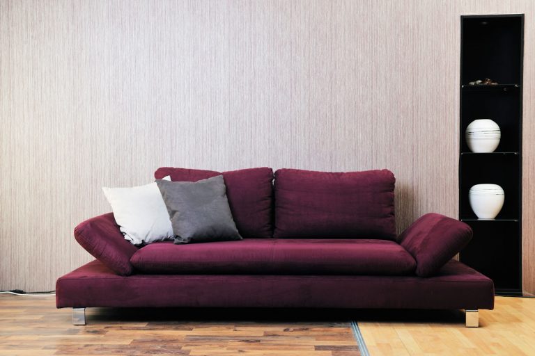 A modern designed burgundy colored sofa with gray and white colored throw pillows