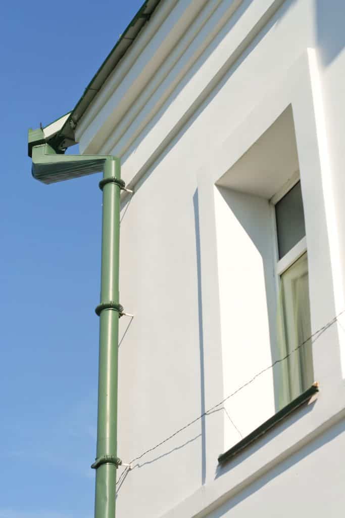 A two storey white house with recessed window and a green painted downspout