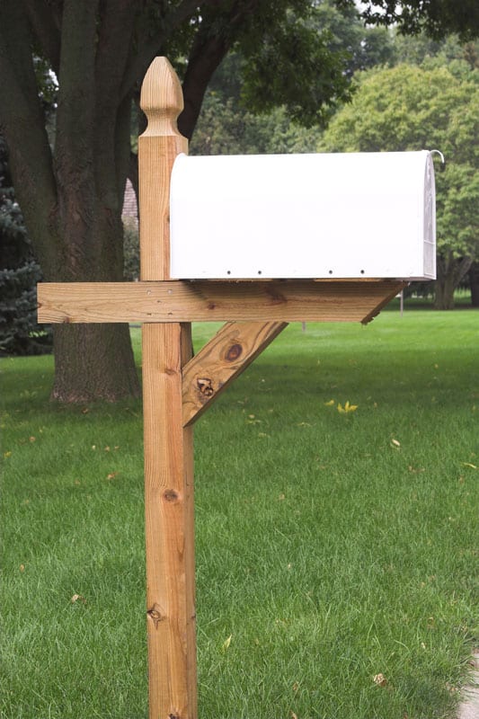A white metal mailbox attached to a wooden post