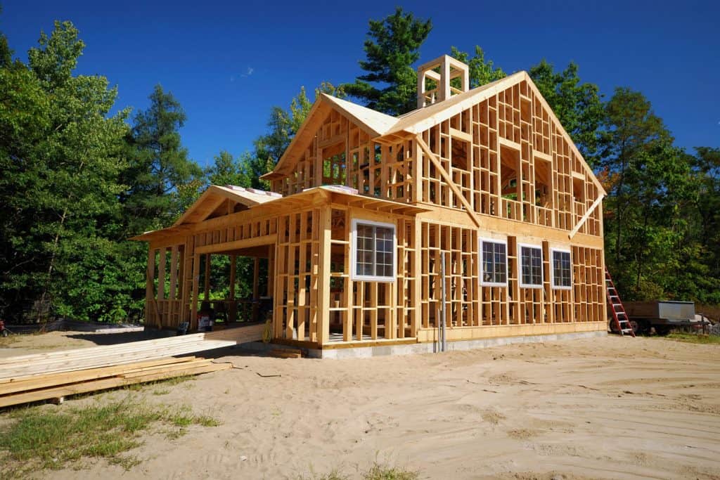 A wooden framing of a house under construction with trees on the background