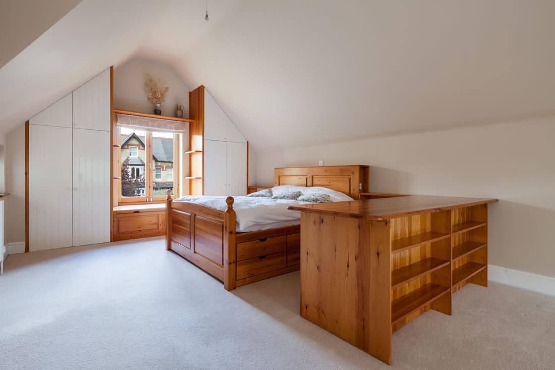 Attic style bedroom with sloping ceilings sparsely furnished with pine bed and cabinets