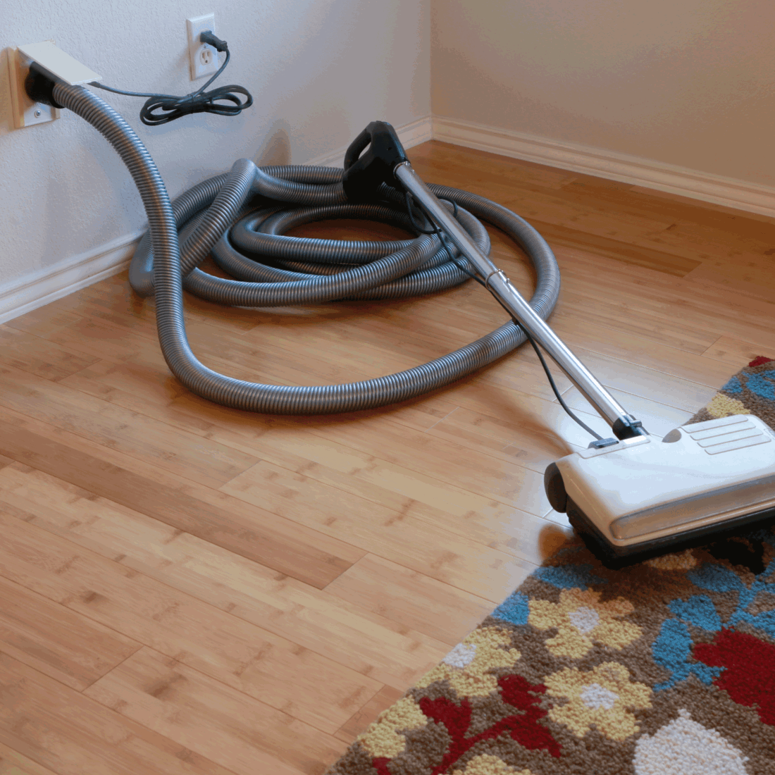 Beautiful bamboo hardwood floor and wool rug with a central vacuum cleaner attached to the wall. How To Store A Central Vacuum Hose