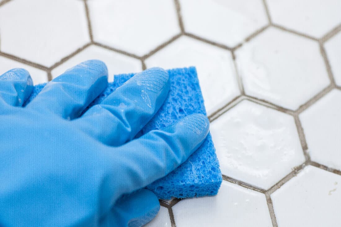 Blue cleaning gloves holding a sponge cleaning a tile floor