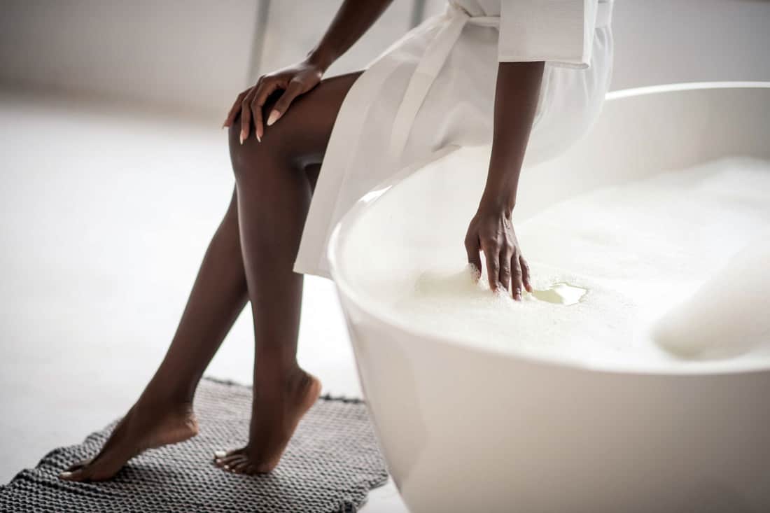 Close up of dark-skinned young woman putting hand in water in bath with foam