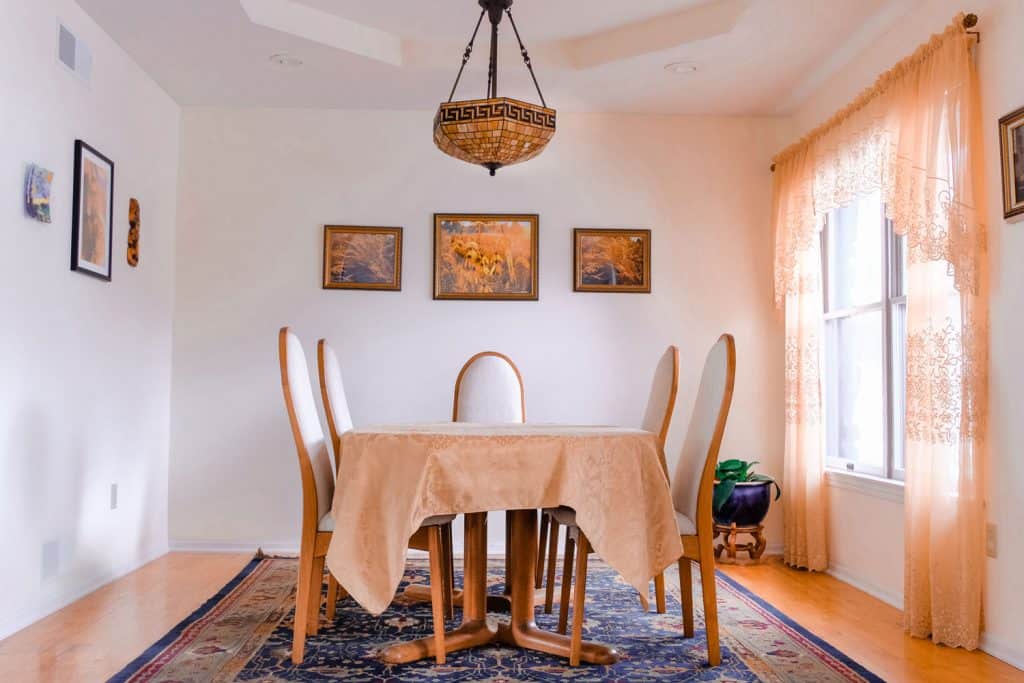 interior of a narrow dining room with an oriental are rug with white chairs and a wooden dining table