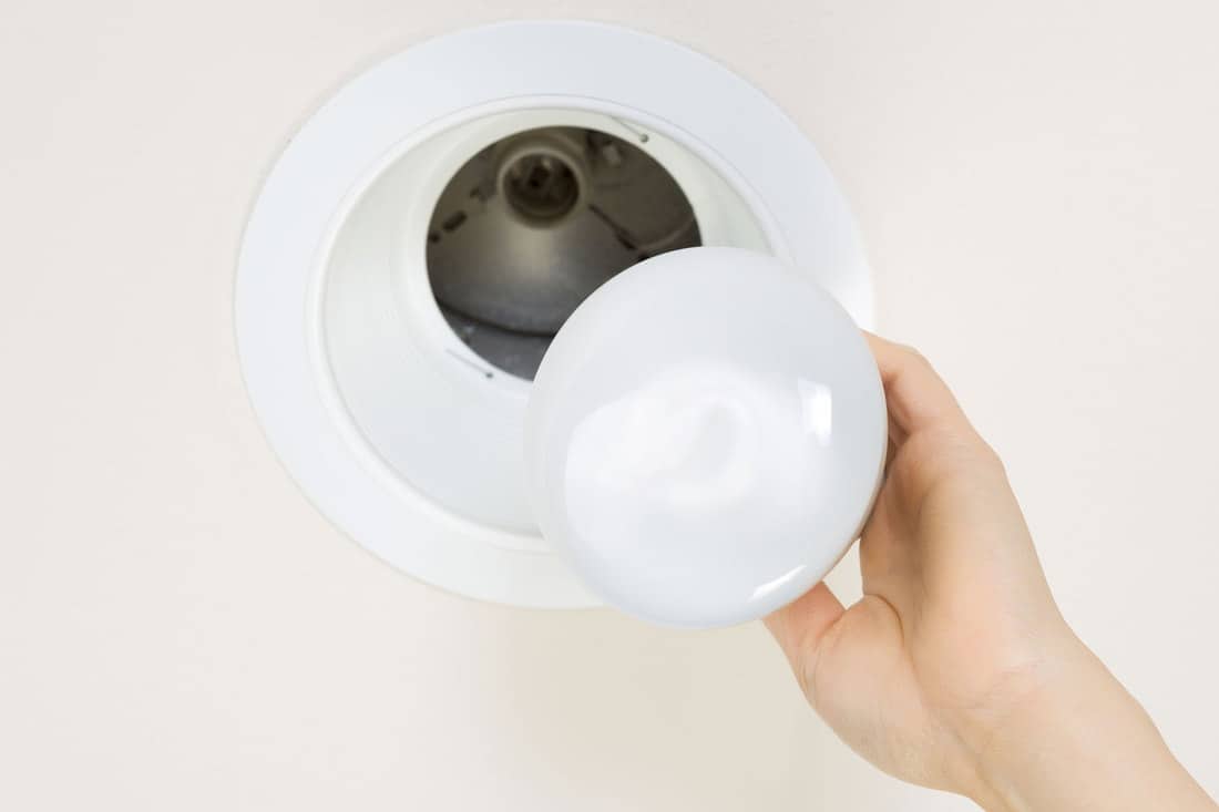 Photo of brand new flood light bulb being held by female hand with recessed ceiling light mount in background