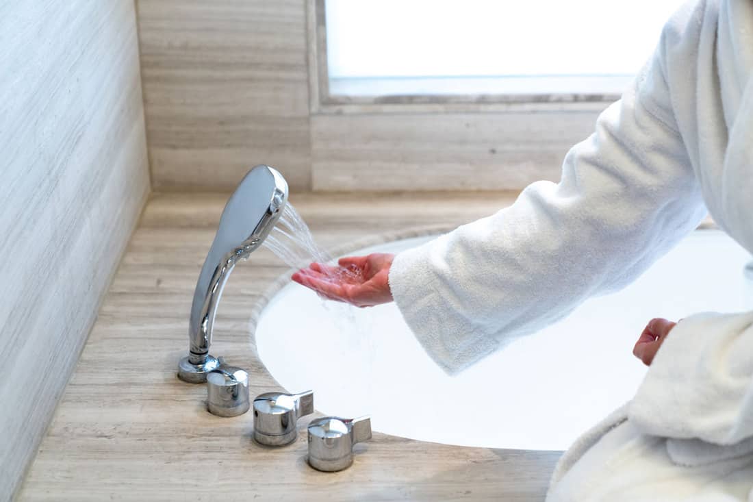 Woman is checking temperature touching running water with hand for having a bath