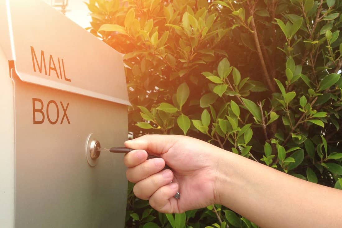 Woman's hand open the mail box with the key in front of house. Use the key to open the mailbox.