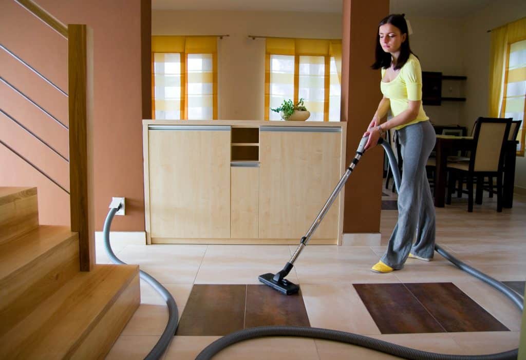 Young woman cleaning floor using a central vacuum system (also known as built-in or ducted vacuum cleaner).