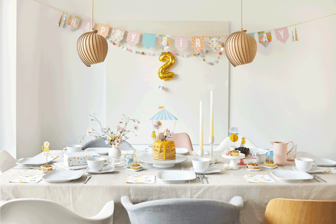 A modern and fresh table decoration with the theme of circus and animals for a children's birthday party with pancake birthday cake, pennant garland, animal figures, balloon, stationery and flowers