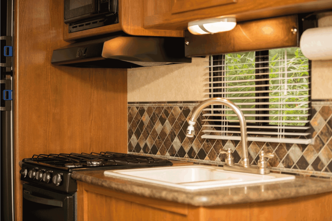 kitchen area inside of a motor home vehicle. Sink, stove, window.