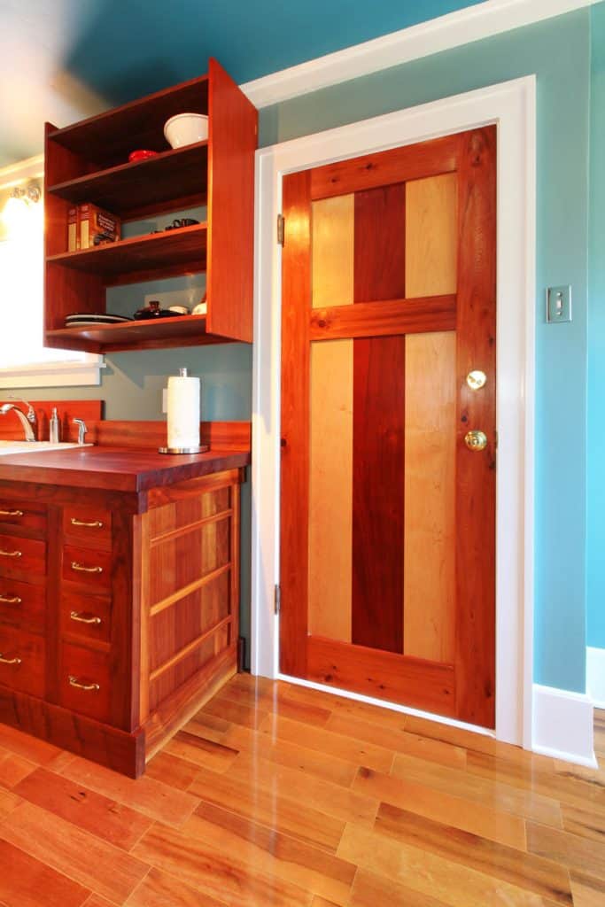 A blue painted living room with wooden flooring, wooden cabinetries, and a huge wooden door