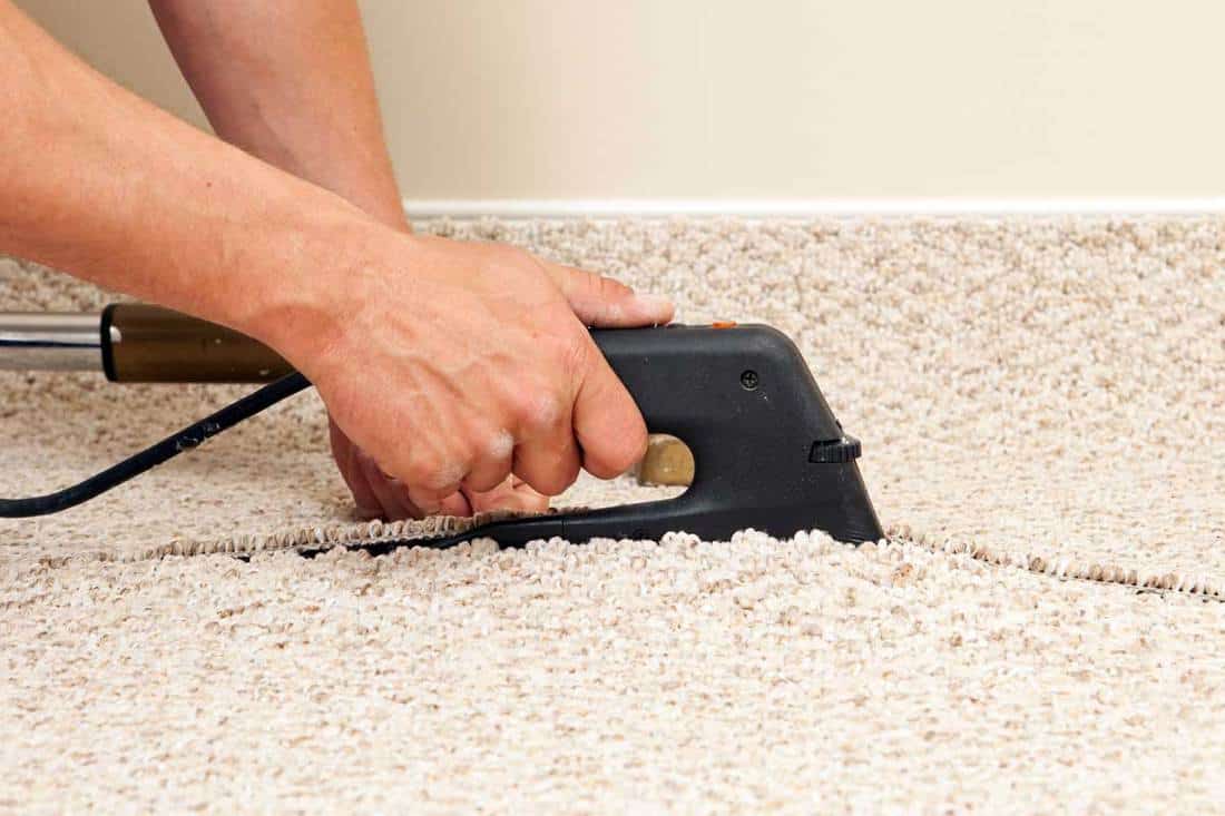 A carpet installer using a seam iron to join two sections of berber carpet in a bedroom, How Hot Does A Carpet Iron Get?