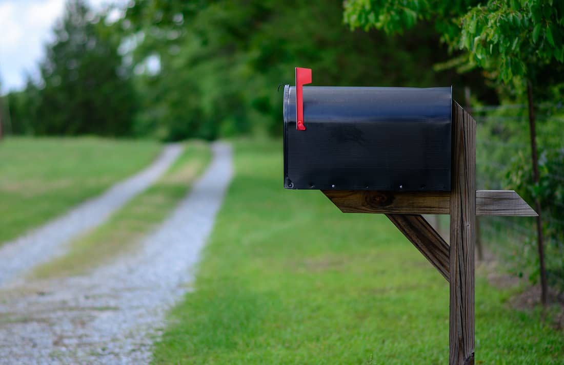 A large black metal mailbox along a quiet country road