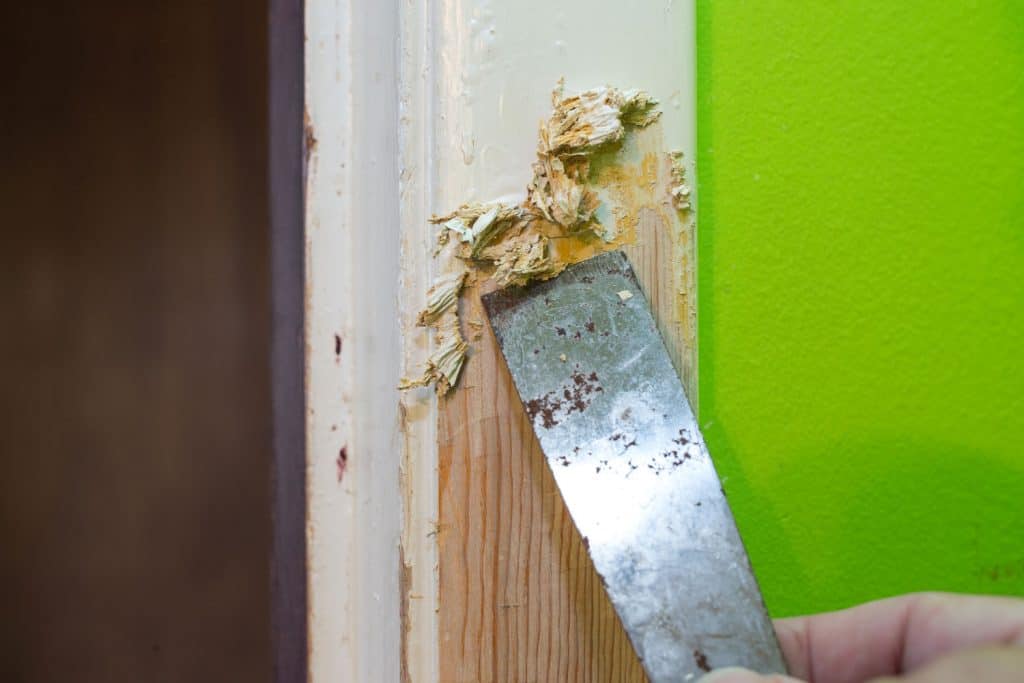 A man removing paint on the door frame