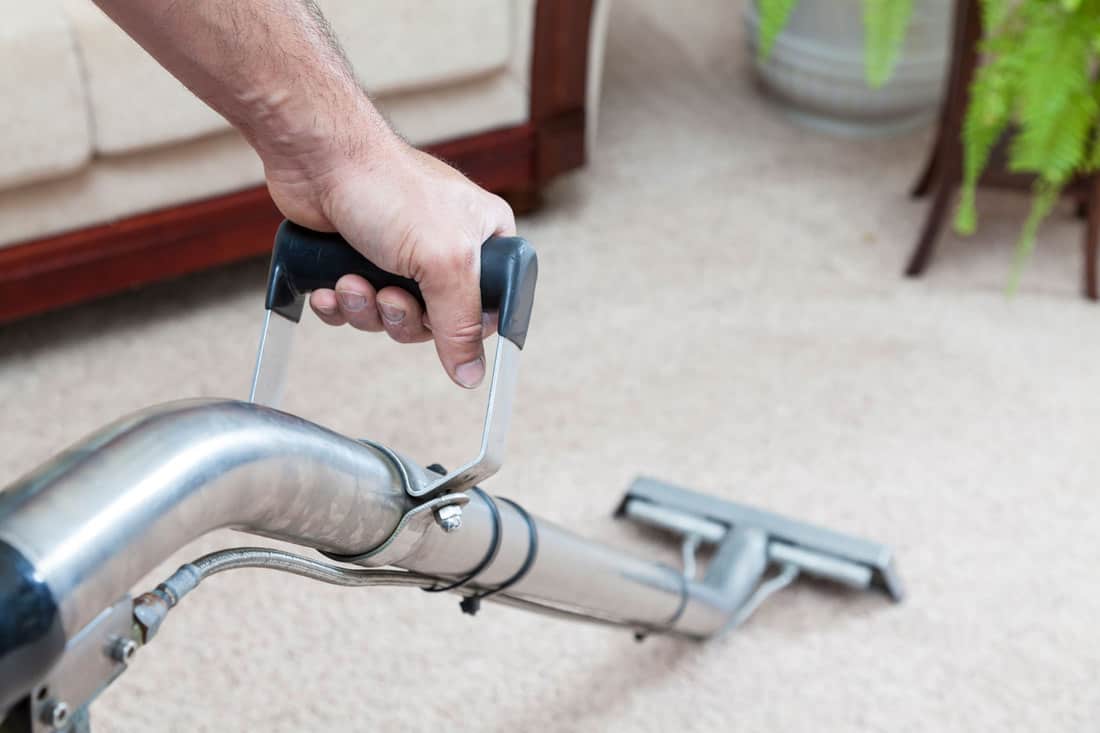 A man steam cleaning the carpet inside his living room, How To Remove Sticky Residue From Carpet Protection Film