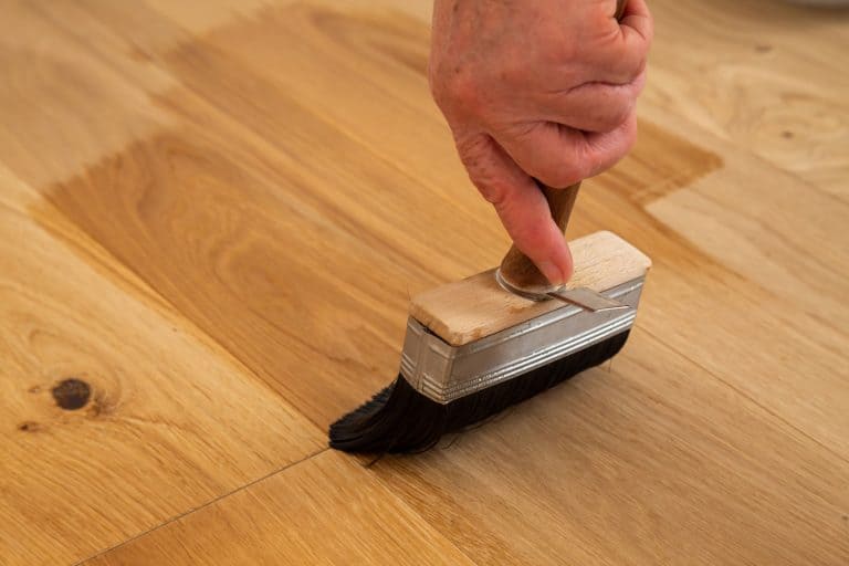 A painted using a brush to clean the wooden tiles before painting, How To Change Hardwood Floor Color [3 Quick Steps To Follow]