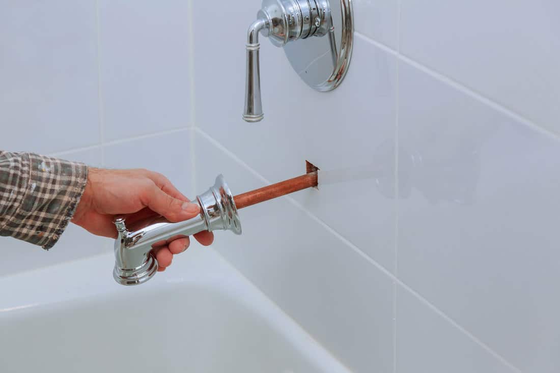 A repair man pulling a faucet pipe out of the bathroom wall, How To Extend A Bathtub Spout Pipe - 2 Methods To Try