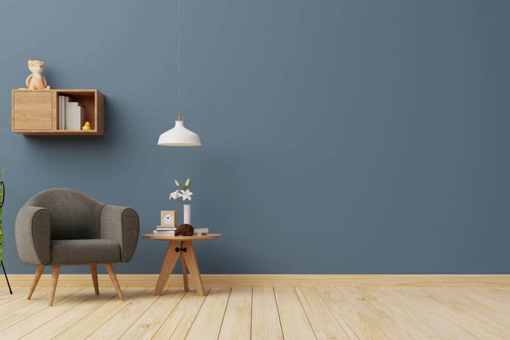 A small gray couch with a wooden end table on the side and a blue accent wall
