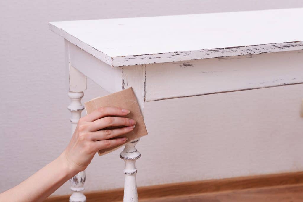 A woman removing paint on the small white table using a sand paper