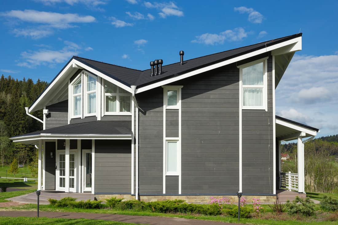 An exterior photo of a huge two storey house with gray wooden sidings and a small garden landscaping outside, What Color Gutters For A Grey House?