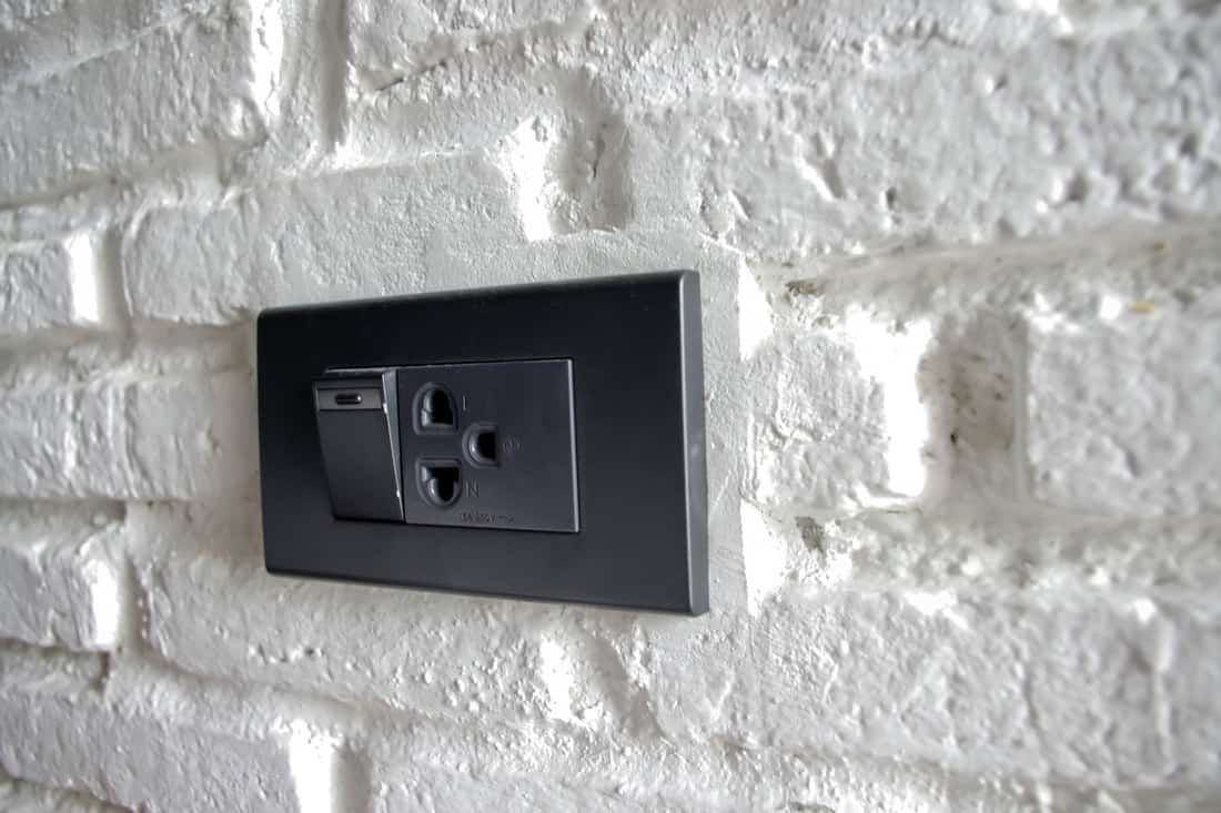 Black Light switch and power socked on white brick wall, What Color Switch Plates And Outlets For White Walls?