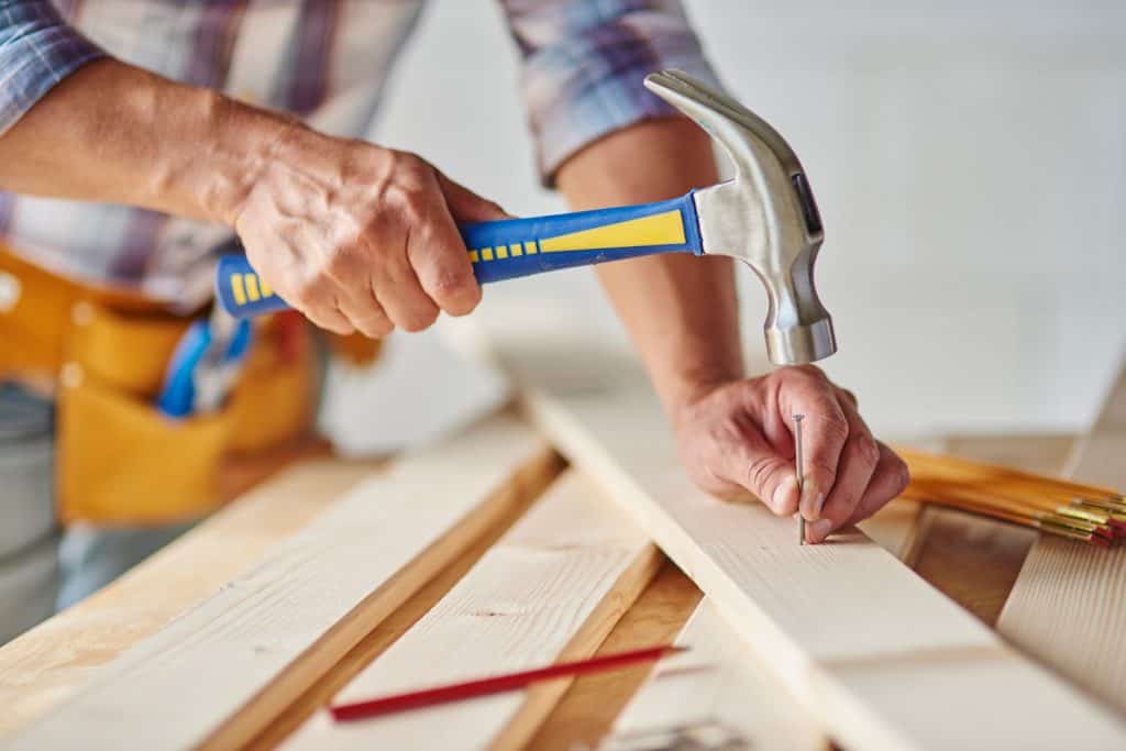 Carpenter with hammer hitting nails, Should You Nail Or Screw Wood Together?