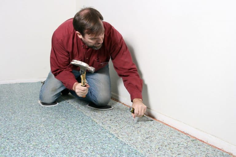Carpet installation with worker bending to chisel at tackless tack strip on carpet pad, How To Install Carpet Padding Under An Area Rug